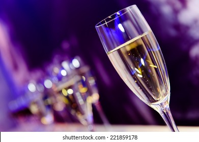 Glass with champagne lit by nightclub lights on dark-purple background