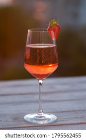 A Glass Of Champagne On The Blurred Natural Background Of The Sunset. A Glass Of Pink Sparkling Wine Close-up On A White Wooden Background. Festive Evening. Soft Focus, Beautiful Bokeh.