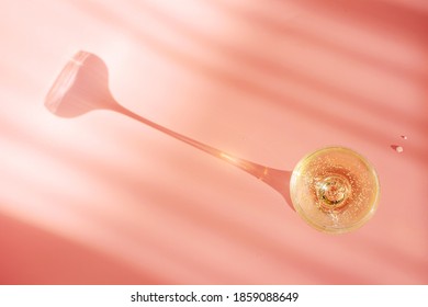 A glass of champagne on a pastel pink background. Bright sunlight, a spectacular long shadow comes from the glass. Creative concept of holiday, celebration, party, alcohol.  