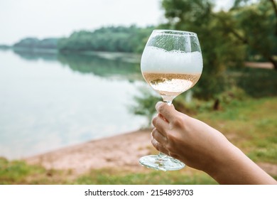 Glass With Champagne In Woman Arm On A Nature Background. Alcoholic Drink With Bubbles And Foam. Summer Picnic. Beach Bachelorette Party Concept. Graduation Celebration Outdoors. Copy Space. Close-up.