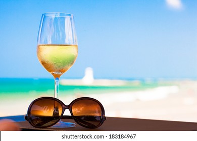 Glass Of Chilled White Wine And Sunglasses On Table Near The Beach