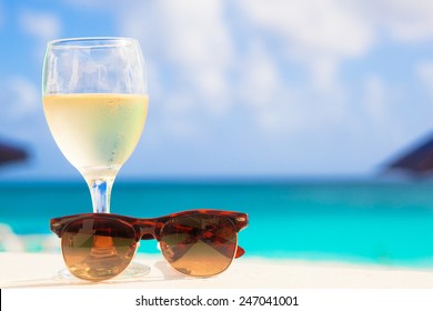 Glass Of Chilled White Wine And Sunglasses On Table Near The Beach