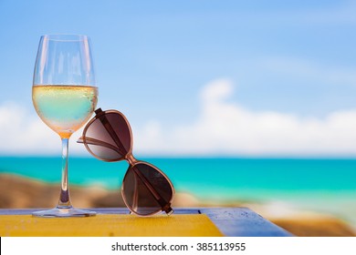 Glass Of Chilled White Wine And Sunglasses On Table Near The Beach