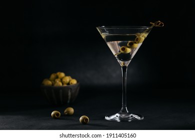 Glass of classic dry martini cocktail with olives on dark stone table against black background. With free space for your text