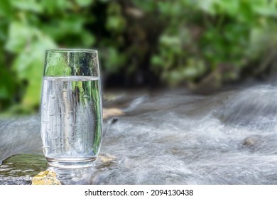 a glass of clean transparent drinking water in a transparent glass on a stone in a green forest near a stream or mountain spring. healthy food and diet, beautiful background copy space - Shutterstock ID 2094130438