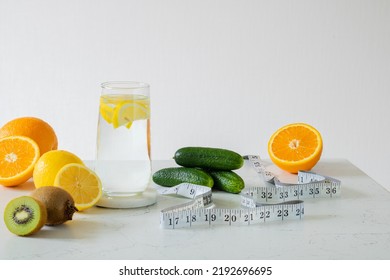 A Glass Of Clean Water With Lemon Slices. Nearby Are Citrus Fruits, Kiwi, Cucumbers And Centimeter. Healthy Food Concept. Losing Weight Concept.