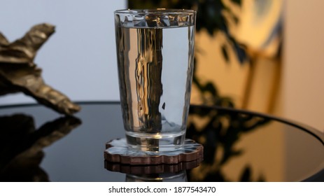 A Glass Of Clear Water Stands On A Black Glossy Table. Transparent Stele, Clean Drinking Water. Evening Light Of Sunset.