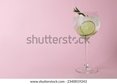 Glass of cocktail with lime on pink background