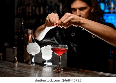 Glass with a cocktail stands on the bar counter, and the bartender's hands squeeze a piece of zest over the cocktail - Powered by Shutterstock