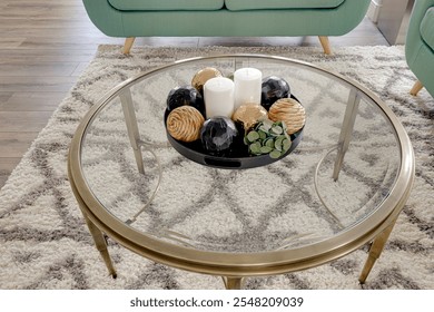 A glass coffee table with a vase of candles and a few balls on it. The table is surrounded by a rug and a couch. Scene is cozy and inviting