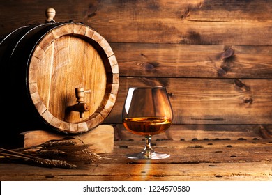 Glass of cognac with barrel on wooden backgroun.
