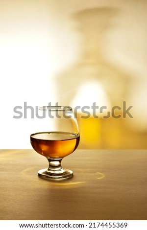 A glass of cognac with bottle shadows on a wooden light table. Cognac or brandy on a light background. copy space. vertical photo 
