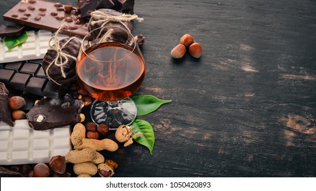 A glass of cognac, brandy, whiskey and a set of chocolate with cookies and sweets. On a black wooden background. Copy space for text.