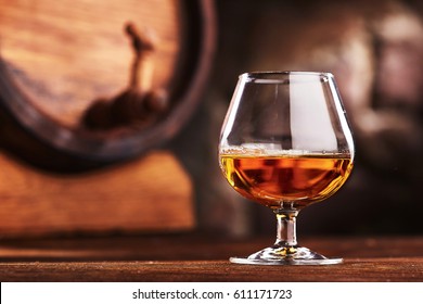 Glass of Cognac and old oak barrel defocussed
