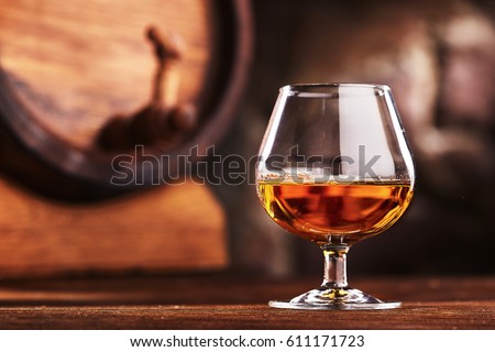 Glass of Cognac and old oak barrel defocussed