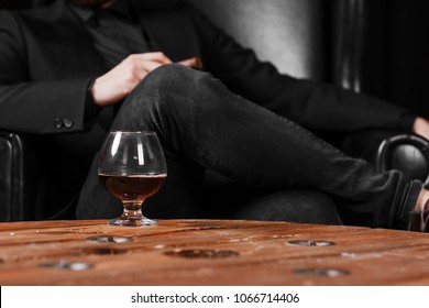 A Glass For Cognac On A Wooden Table On The Background Of A Leather Chair.