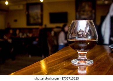 A glass of cognac stands at the bar, against the backdrop of visitors to the cafe