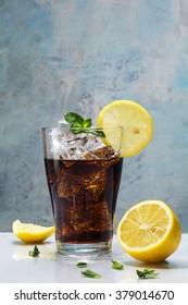 glass of cola or coke with ice cubes, lemon slices and peppermint garnish against a blue vintage wall,  copy space, selected focus 
