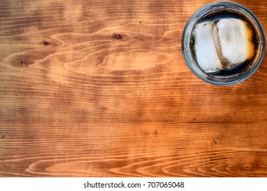 Glass Of  Cola And Ice Slice From Above In The Up Right Corner Of Wooden Table