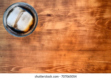 Glass Of  Cola And Ice Slice From Above In The Up Left Corner Of Wooden Table