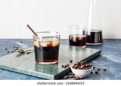 Glass of cold brew with straw and coffee beans on color table against white background