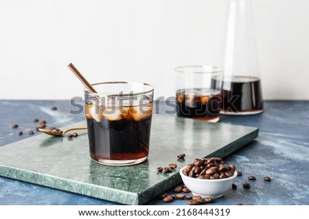 Glass of cold brew with straw and coffee beans on color table against white background