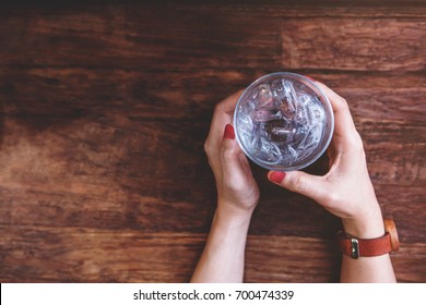 Glass Of Cold Water With Ice In Hipster Woman Hand Lay On Wooden Table, Top View