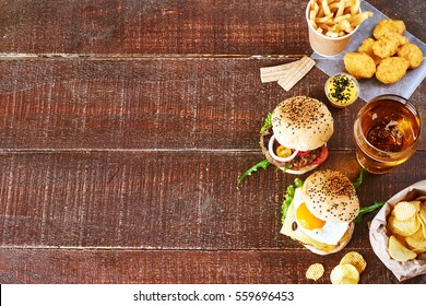 Glass of cold wheat beer and snack set: beef burgers, chicken nuggets, french fries, potato  chips on a brown wooden table. Copy space. - Powered by Shutterstock