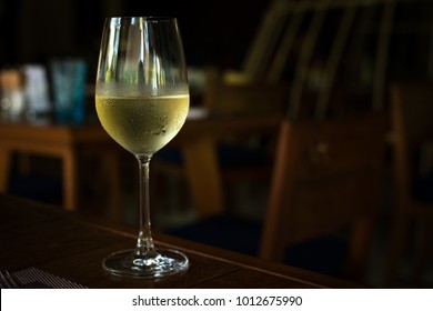 Glass with cold white wine on table at restaurant interior, nobody