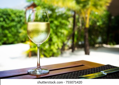 Glass With Cold White Wine On Wooden Table On Tropical Background