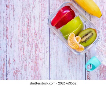 Glass Container Lunch Box Fresh Fruit With Apple, Kiwi,  Orange And Banana, Water Bottle On Light Blue Wooden Background. Take Away Food. Top View With Copy Space, Healthy Eating Concepts.
