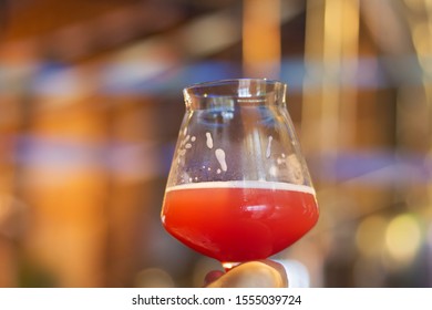 A Glass Of Craft Beer With Infused Raspberry Flavor During Testing Event In Burlington, Vermont, USA. Background Hues Of Festive Autumn Atmosphere In A Bar.