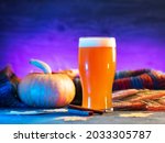 A glass of craft pumpkin beer ale. Fresh pumpkin, knitted colorful autumn warm scarf, rye ears, cinnamon sticks and neon background