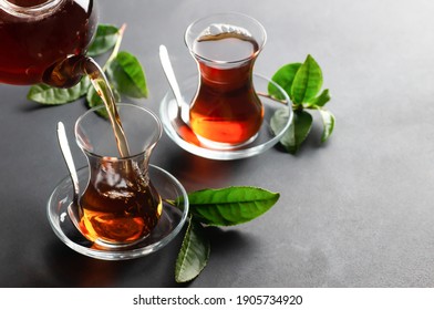 Glass Cup Of Black Tea Pouring From Teapot With Fresh Tea Leaves, Traditional Turkish Brewed Hot Drink