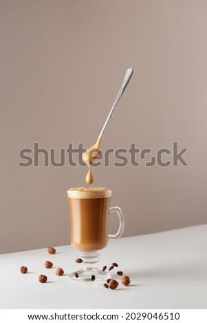 Glass cup with cappuccino and fragrant foam and spoon, hazelnuts and roasted coffee beans.  Creative design for cafes and restaurants with a cup of coffee. 