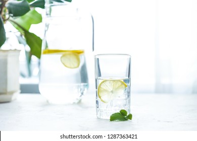 glass cup and a carafe of water, ice, mint and lemon on a white table - Powered by Shutterstock