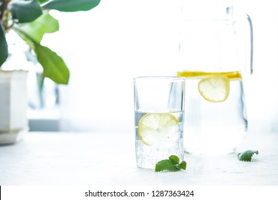 Glass Cup And A Carafe Of Water, Ice, Mint And Lemon On A White Table