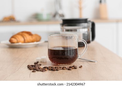 Glass cup of coffee and beans on wooden counter in kitchen, closeup