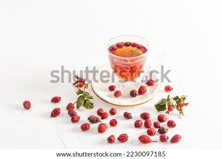 glass cup with double bottom with vitamin hot tea from rose hips on a white background among the berries. useful tea for colds, increased immunity