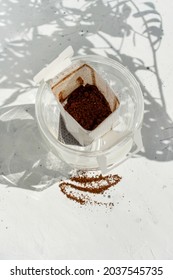 Glass cup with drip coffee bag on white background with shadow and copy space. Opened Instant paper sachet. Trendy hot beverage home brew. Fresh espresso bags still life
