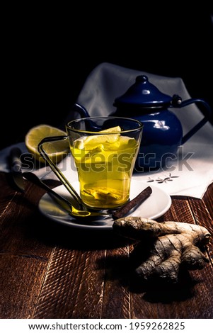 Glass cup with ginger and lemon tea, on wooden table and blue teapot. Concept of homeopathy and traditional medicine