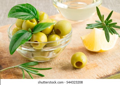 Glass cup with green pitted olives decorated with herbs and rosemary on a wooden base with a shallow depth of focus. - Powered by Shutterstock