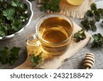 A glass cup of herbal tea with fresh stinging nettles on a table