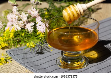 A glass cup with honey on a background of wildflowers. Honey with herbs. Health and benefits