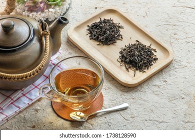 Glass Cup Of Hot Aromatic Black Tea On White Mulberry Paper.Thyme Herbal Tea, View From Above Top. Glass Cup Of Tea With Steam On A Serving Tray On  Table With Pot And Dry Tea Leaves For Break .