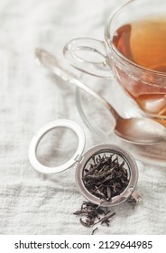 Glass Cup With Hot Black Tea And Infuser With Loose Tea On White Kitchen Towel