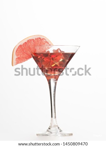 Glass cup with ice stones and drink in coral color with a slice of grapefruit on the rim of the bowl on a white background