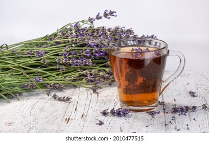 A glass cup with lavender tea on a light wooden table top on a background of lavender flowers. Selective focus, light background - Powered by Shutterstock