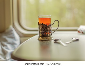 A Glass Cup With Tea In An Iron Cup Holder Is On The Table In The Train Carriage By The Window. Travel Hot Drink. Travel Concept.