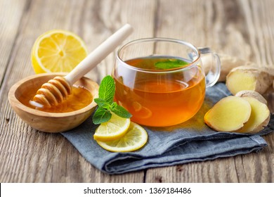 A glass cup of tea with lemon, mint, ginger and honey on wooden rustic table.